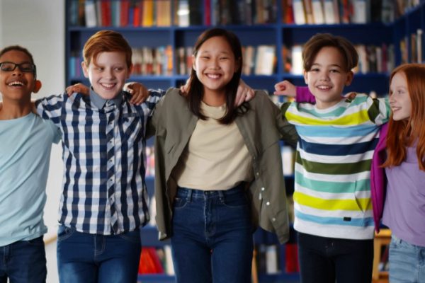 Group of children standing in a library with arms round shoulders