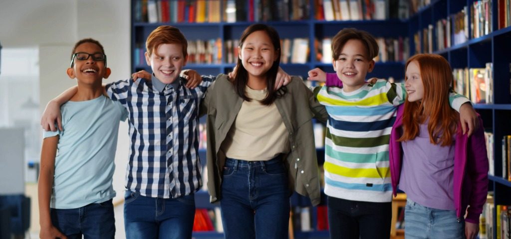 Group of children standing in a library with arms round shoulders