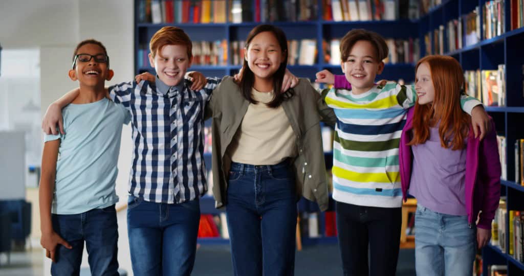 Group of children standing in a library with arms round shoulders