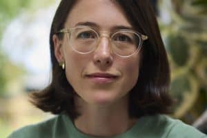 woman with brown shoulder length hair and glasses wearing green sweatshirt