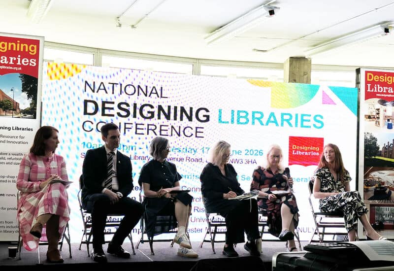panel discussion showing 6 people sat on chair in front of screen saying national designing libraries